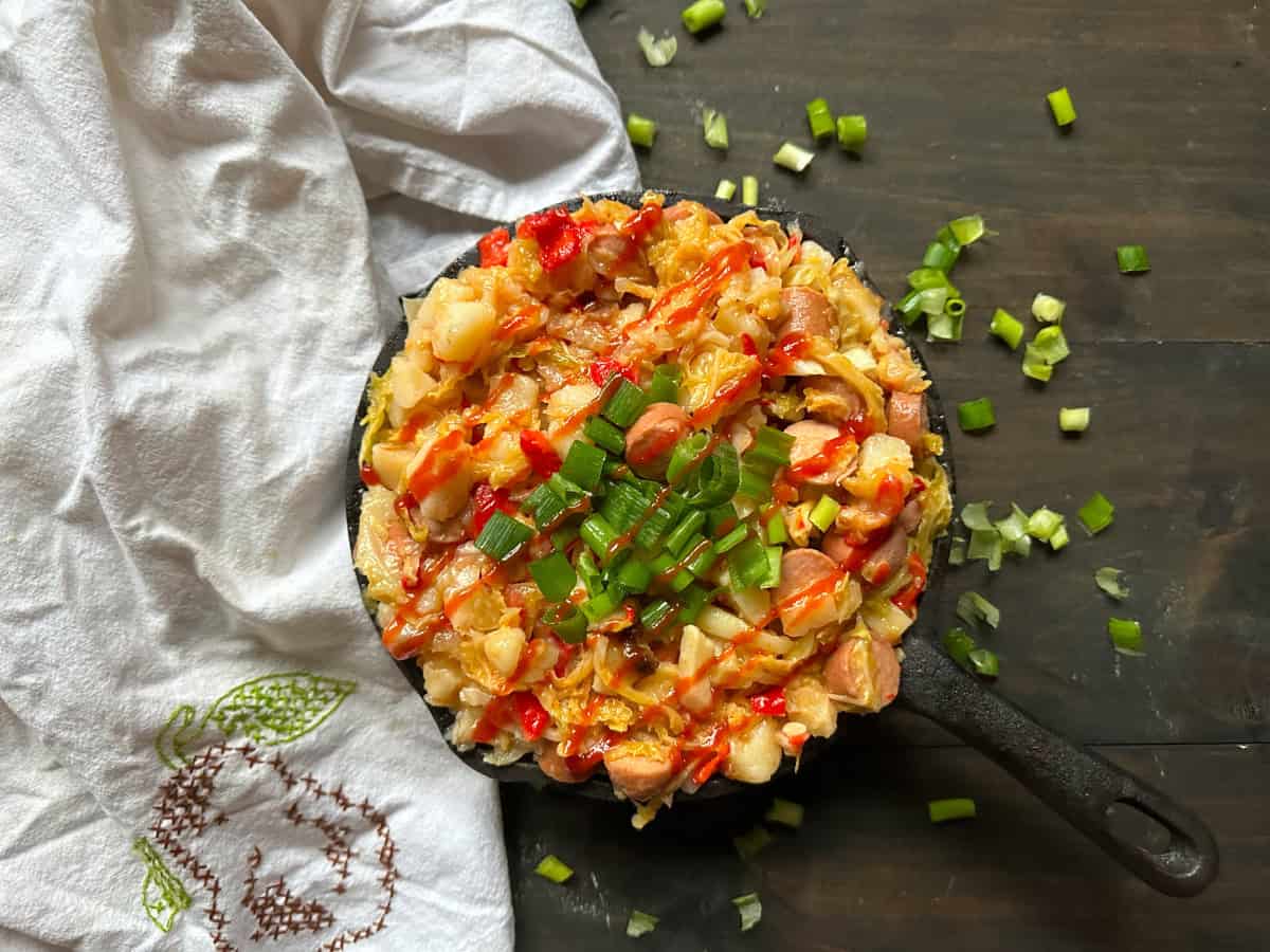 A dish of hot dog hash with a towel and green onions.
