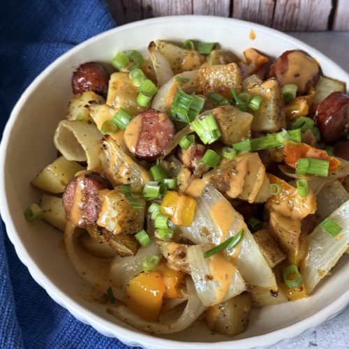 A bowl of kielbasa baked topped with sauce and green onions.