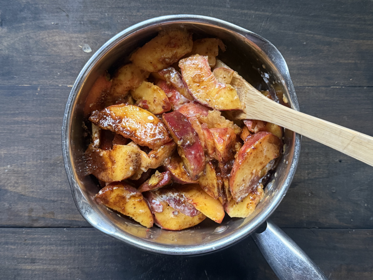 The peaches, sugar, and flour being cooked in a pan, with a wooden spoon.
