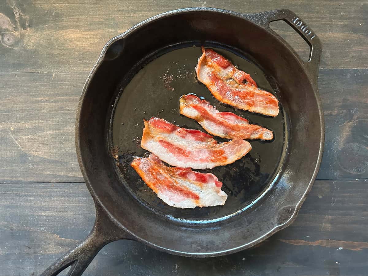 Bacon slices cooking in a cast iron pan.