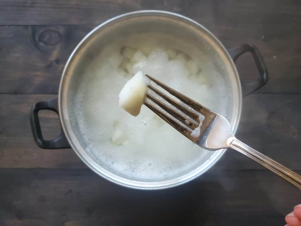 A fork piercing a potato chunk over the potatoes in the boiling water.