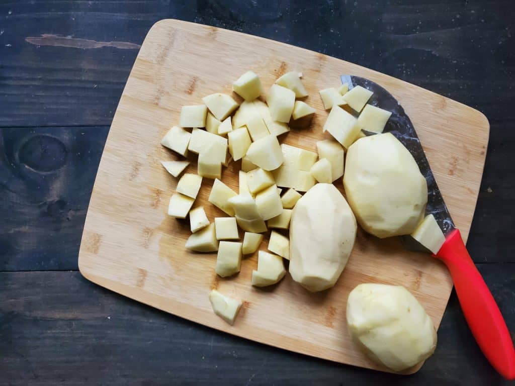 An overhead view of some whole and some chopped potatoes on a cutting board, near a red knife.