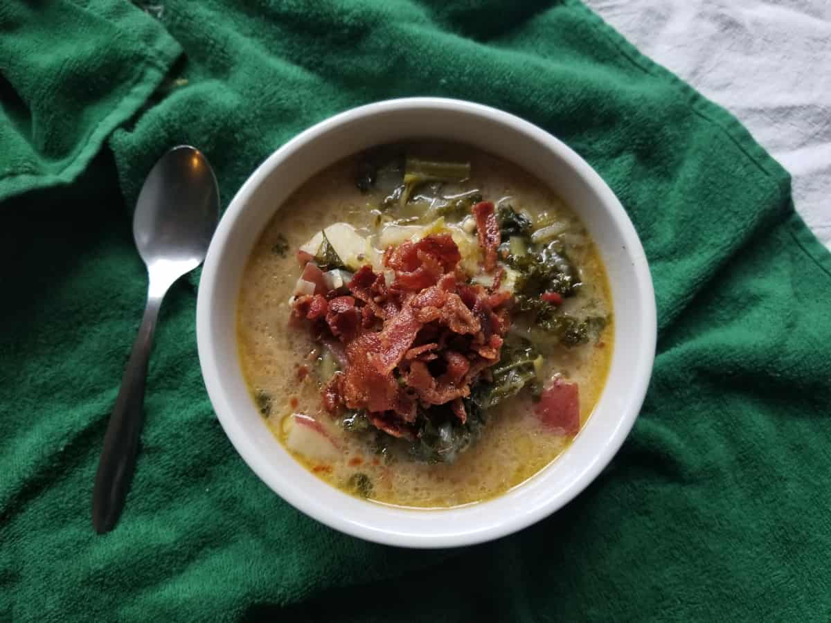 A bowl of potato leek and bacon soup with a spoon.