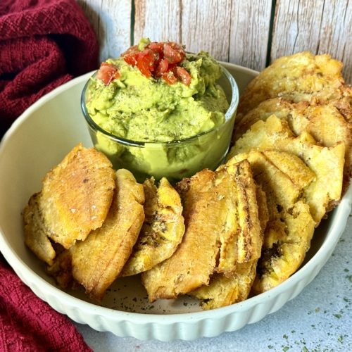 A bowl of tostones and guacamole garnished with tomatoes.