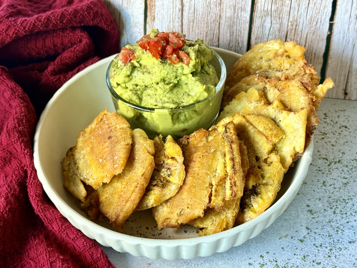 A bowl of tostones and guacamole garnished with tomatoes.
