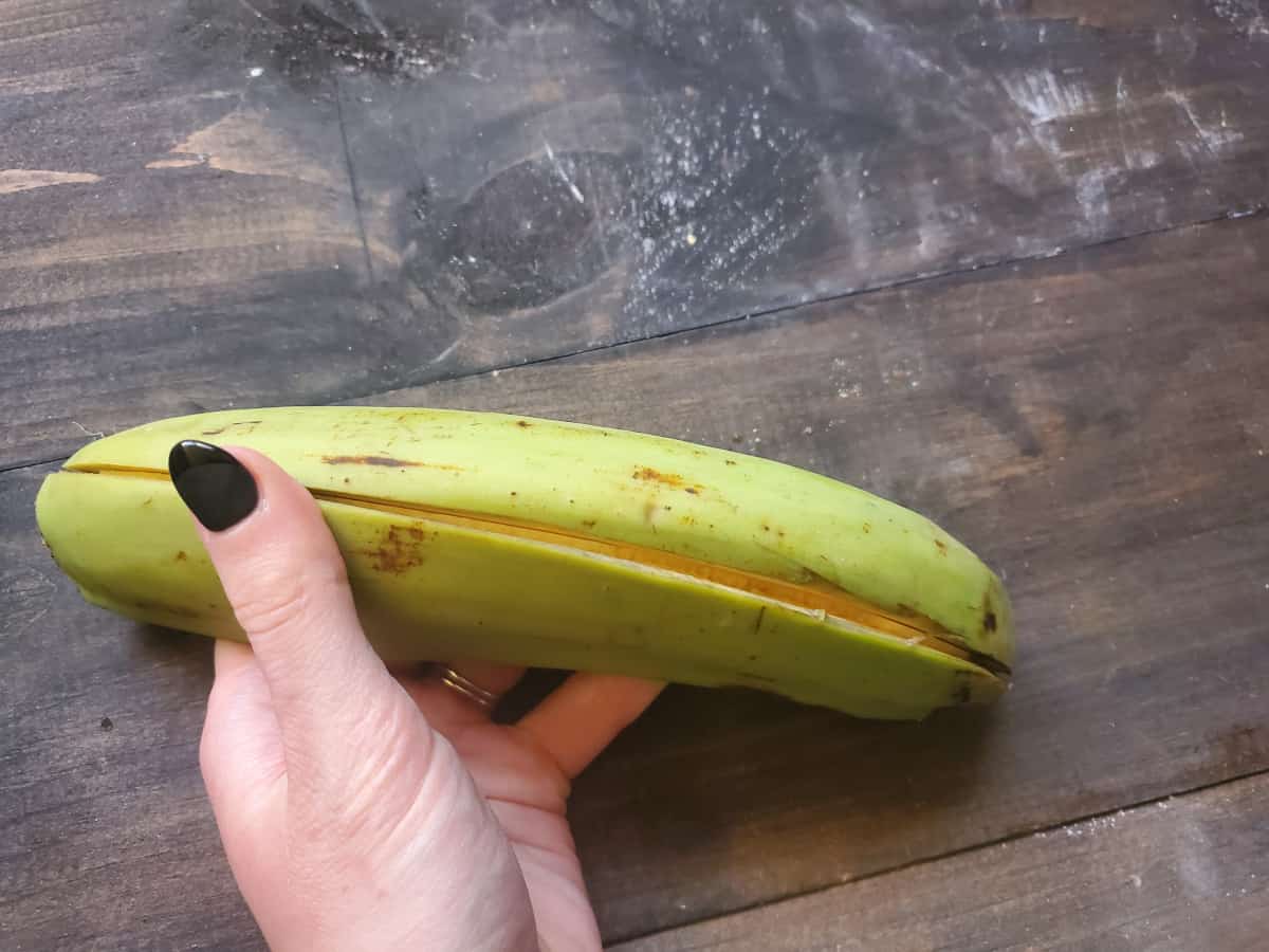 A green plantain sliced open but with the skin still on.