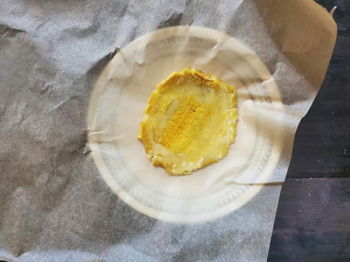 A plantain smashed on parchment paper on a plate.