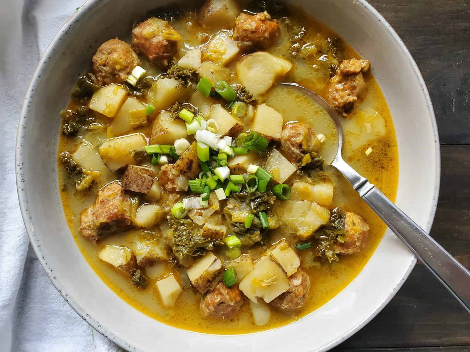 A bowl of dairy free zuppa toscana soup with a spoon and topped with greens.