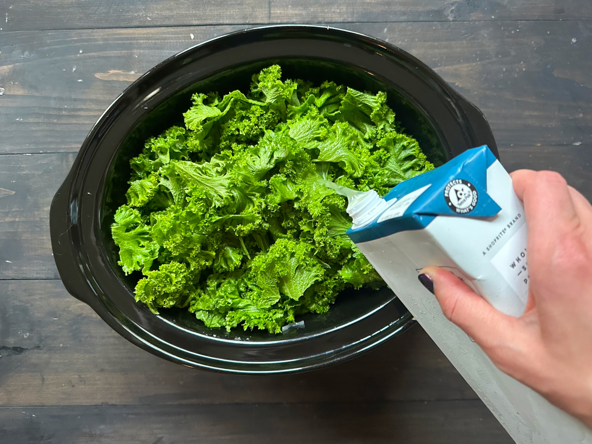 A crockpot filled with kale and broth being added to it.