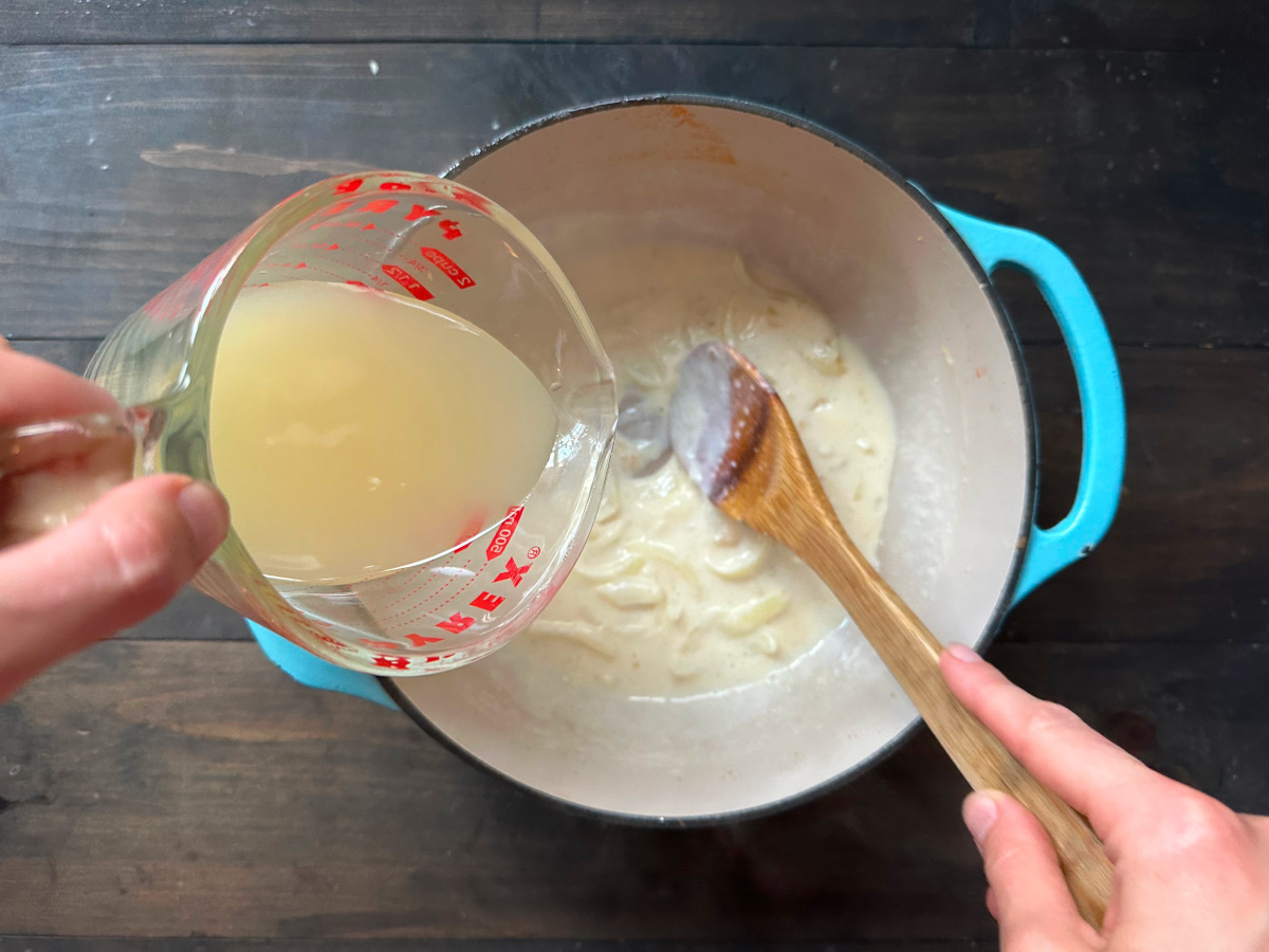 The broth being added to the onion and garlic mixture that's thickened with milk.