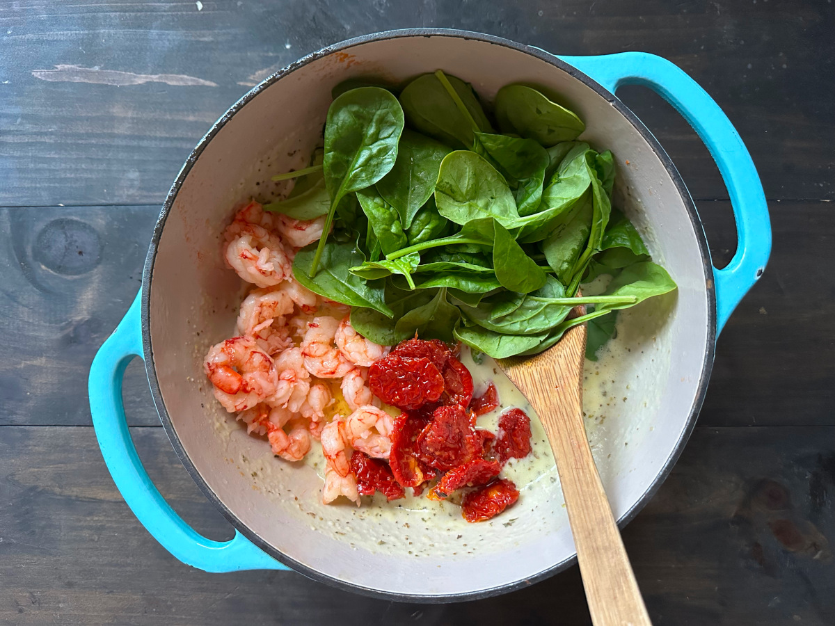 The shrimp, spinach, and tomatoes added to the onion mixture with a wooden spoon.