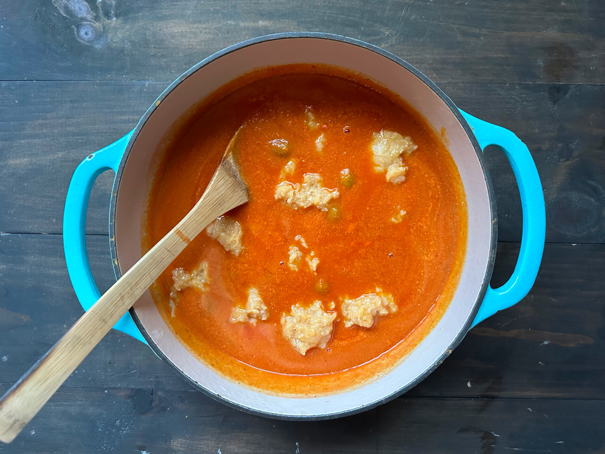 The raw meatballs placed into the sauce with a wooden spoon to coat them.