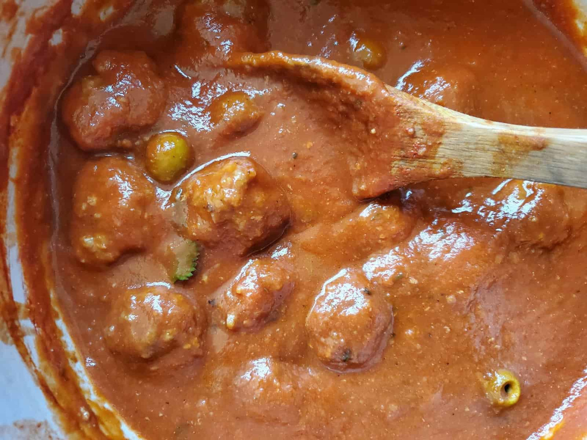 The meatballs cooking in the sauce.