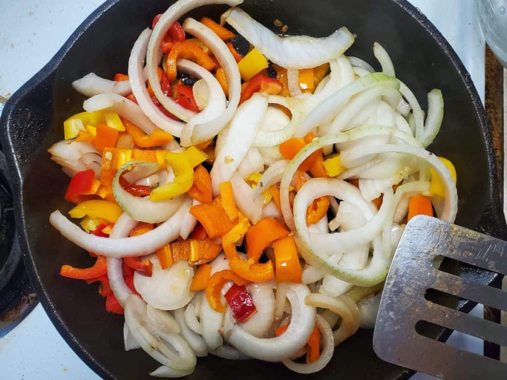 the peppers and onions cooking in a cast iron skillet