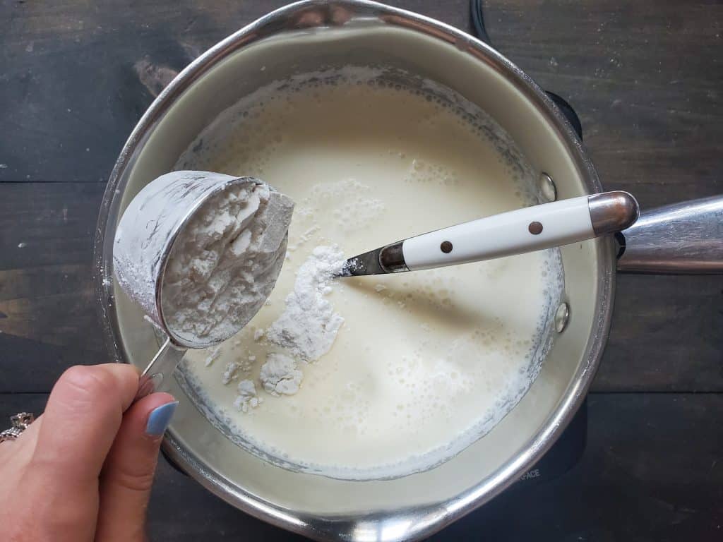 A hand holds a measuring cup emptying the cake mix into the mixture.