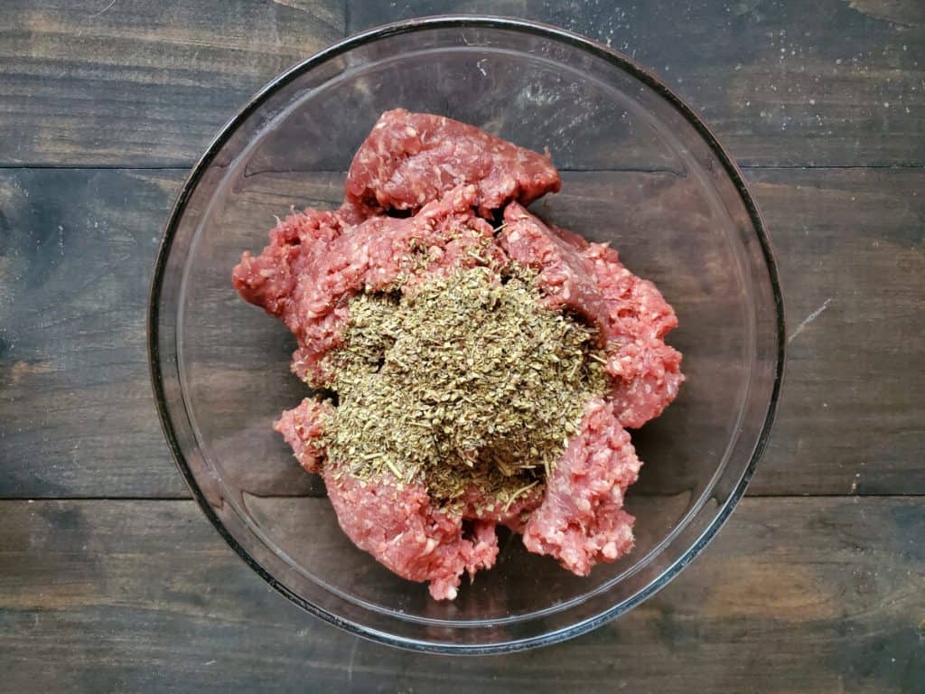 A clear bowl containing ground beef and spices.