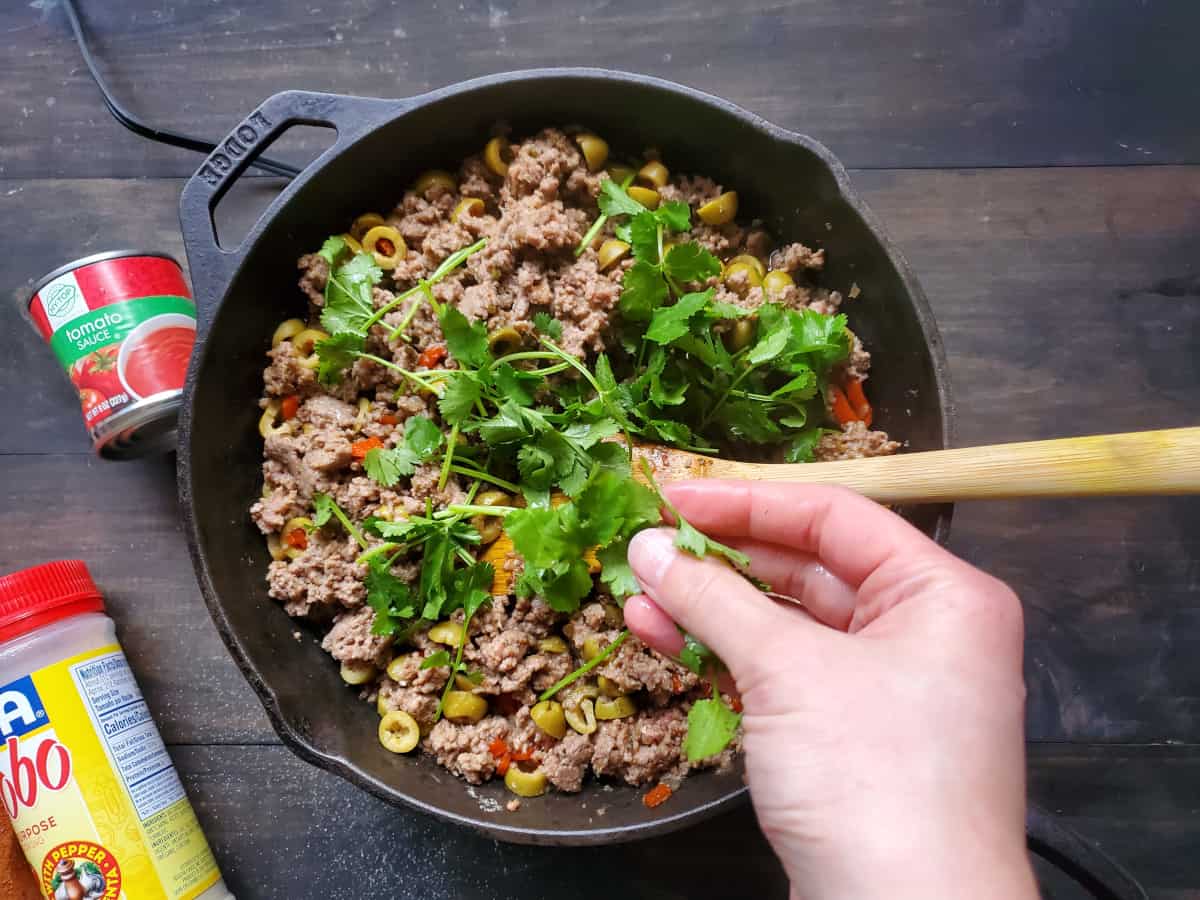 The cilantro being added to the meat mixture.