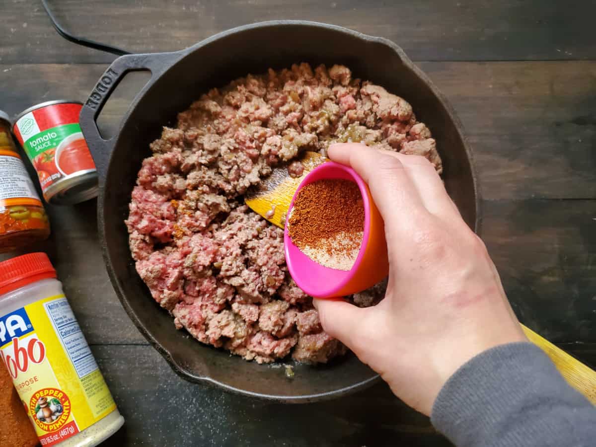 The seasonings being added to the ground beef mixture in the skillet.