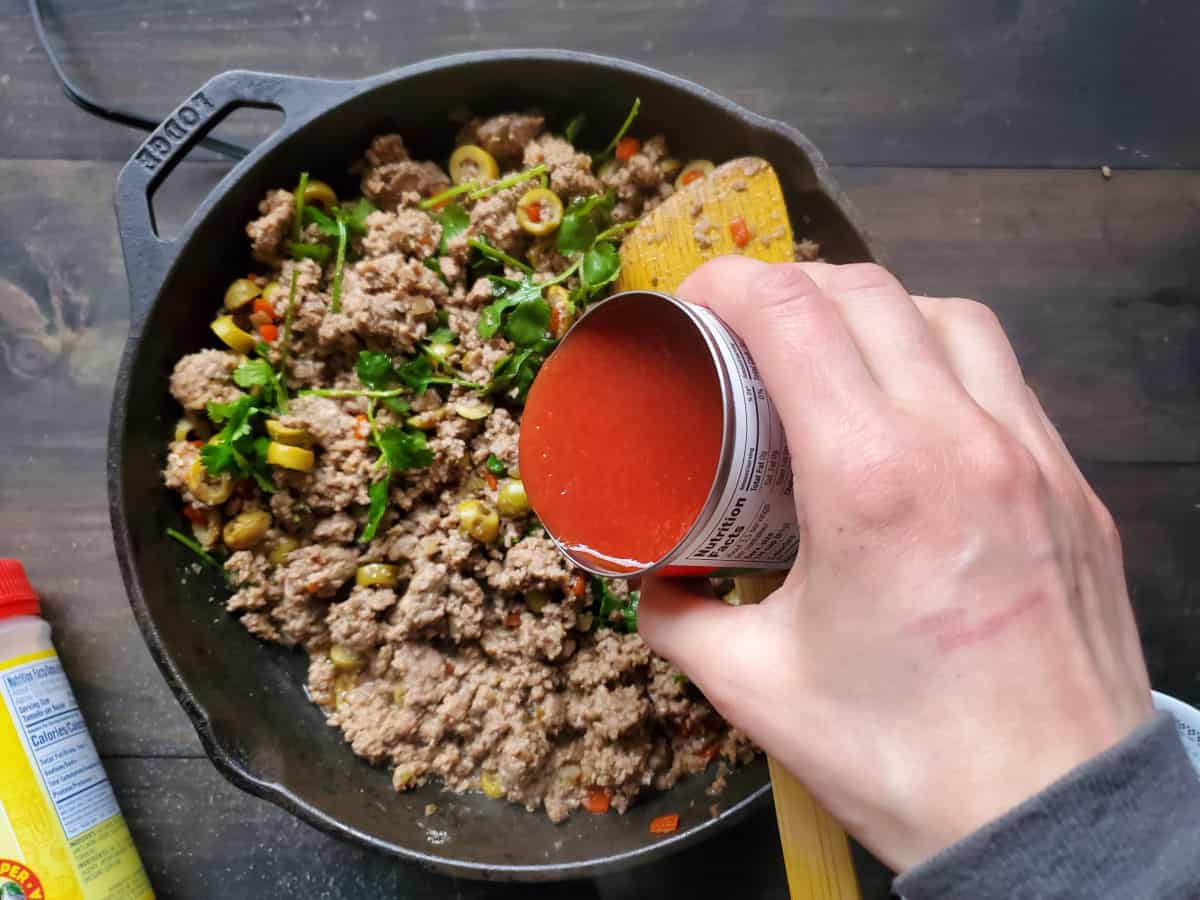 Adding the tomato sauce to the skillet with the meat mixture.
