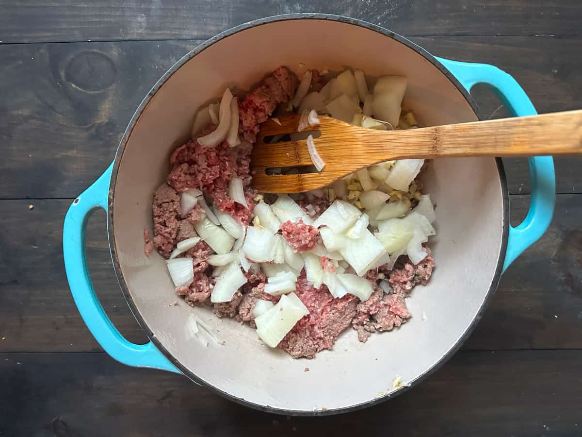 Beef and onion cooking in a pot with a wooden spoon.