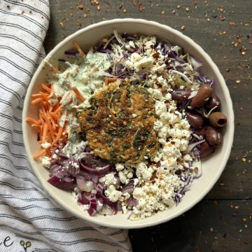 A chicken feta spinach burger in a bowl on top of a salad.