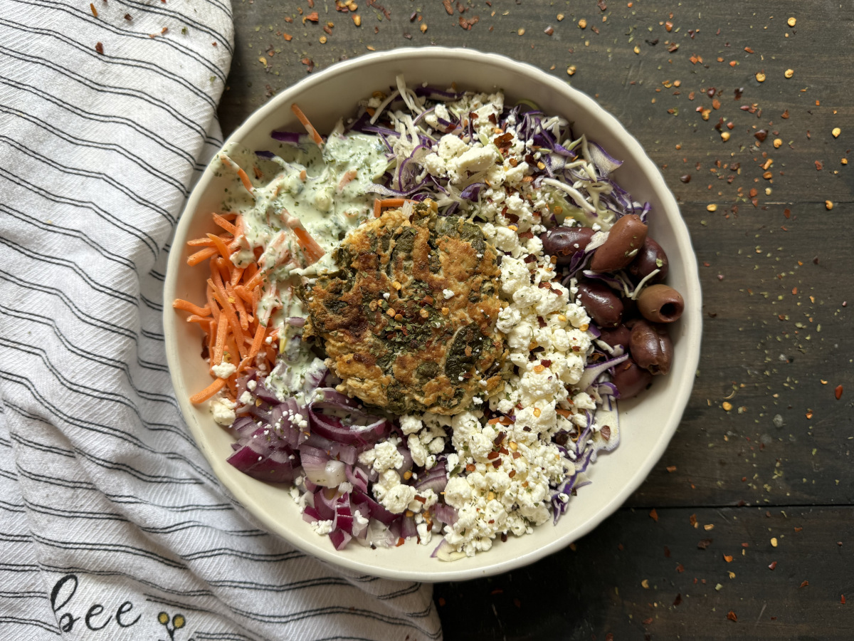 A chicken feta spinach burger in a bowl on top of a salad.