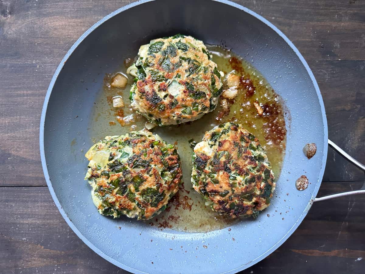 A fry pan with the burgers cooking.