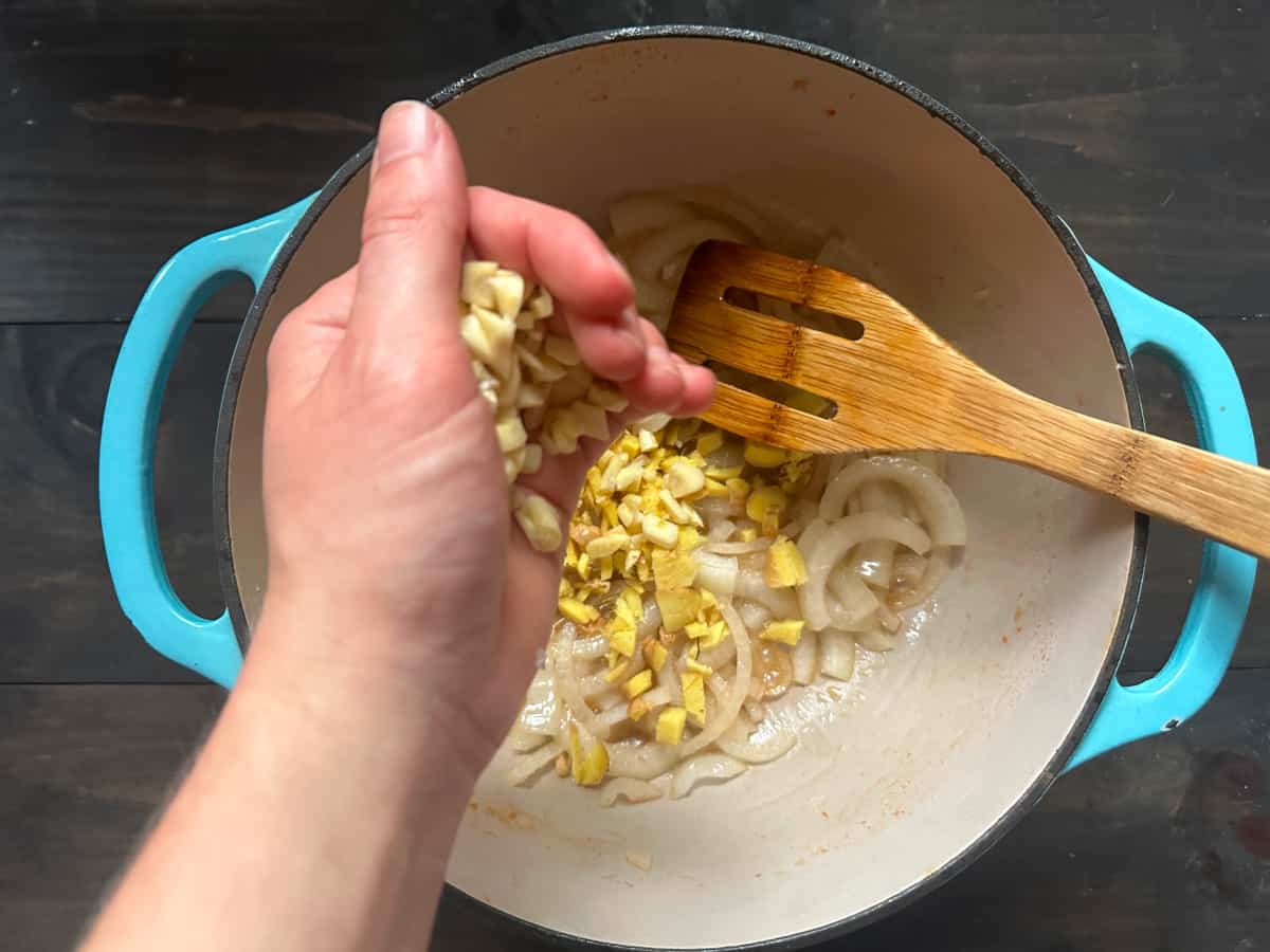 The garlic being added to a pan with ginger and onions.