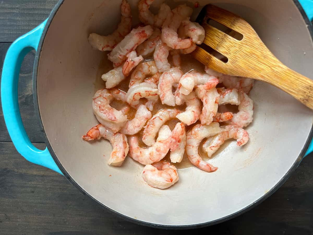 The shrimp cooking in a bowl with a wooden spoon.