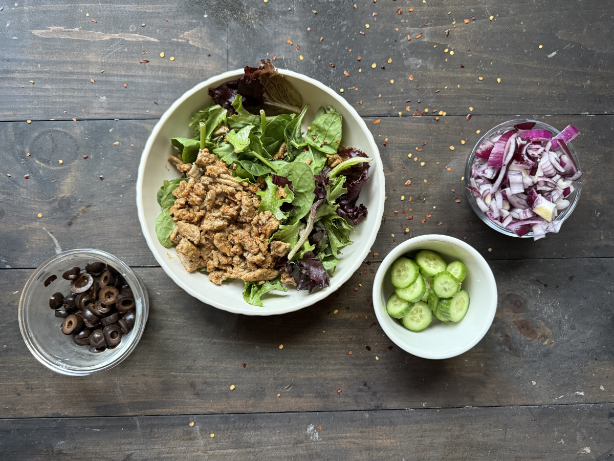 A bowl of greens and turkey surrounded by the toppings.