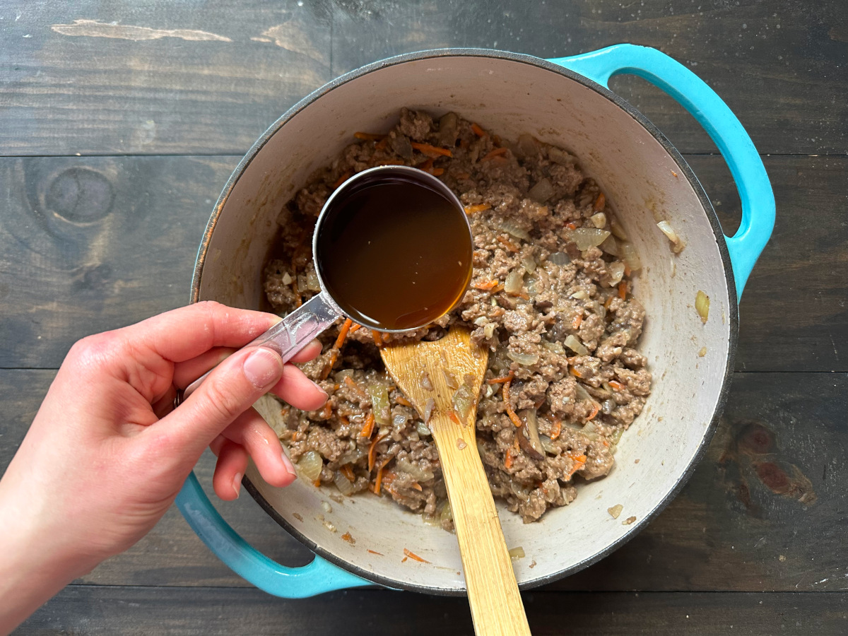 Adding the broth to the cooking meat mixture.