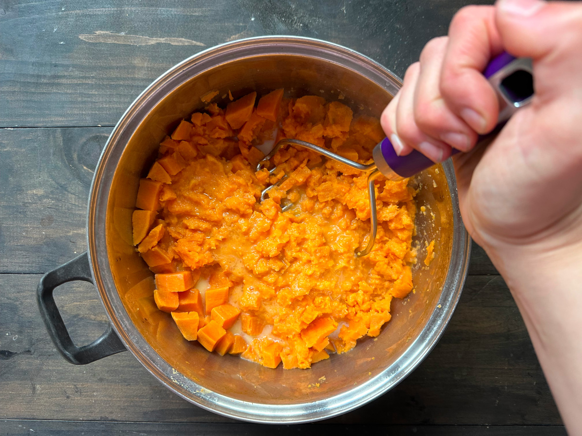 The boiled sweet potatoes being mashed with a hand masher.