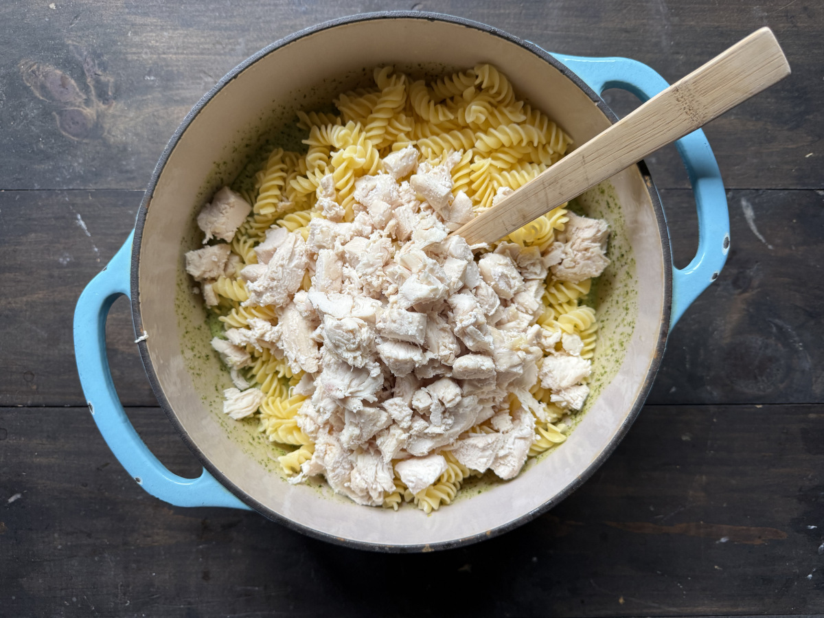 A pot with the pasta and chicken added into the pesto sauce.