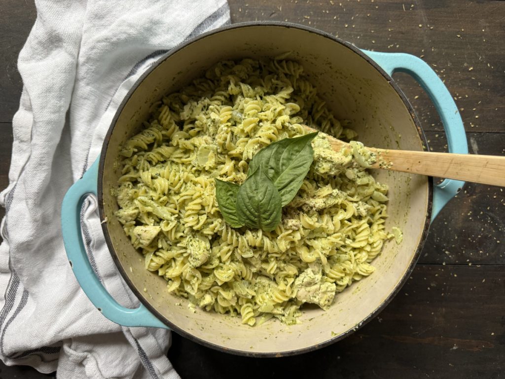 A dish of Gluten Free Chicken Pesto Pasta with a garnish of basil and a spoon.