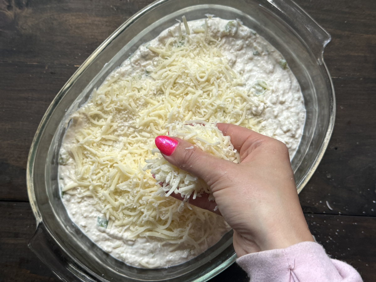 More cheese being added to the top of the dish.