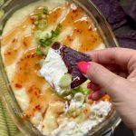 A chip dipped in healthy crab rangoon dip, held over the dip.