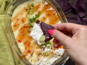 A chip dipped in healthy crab rangoon dip, held over the dip.