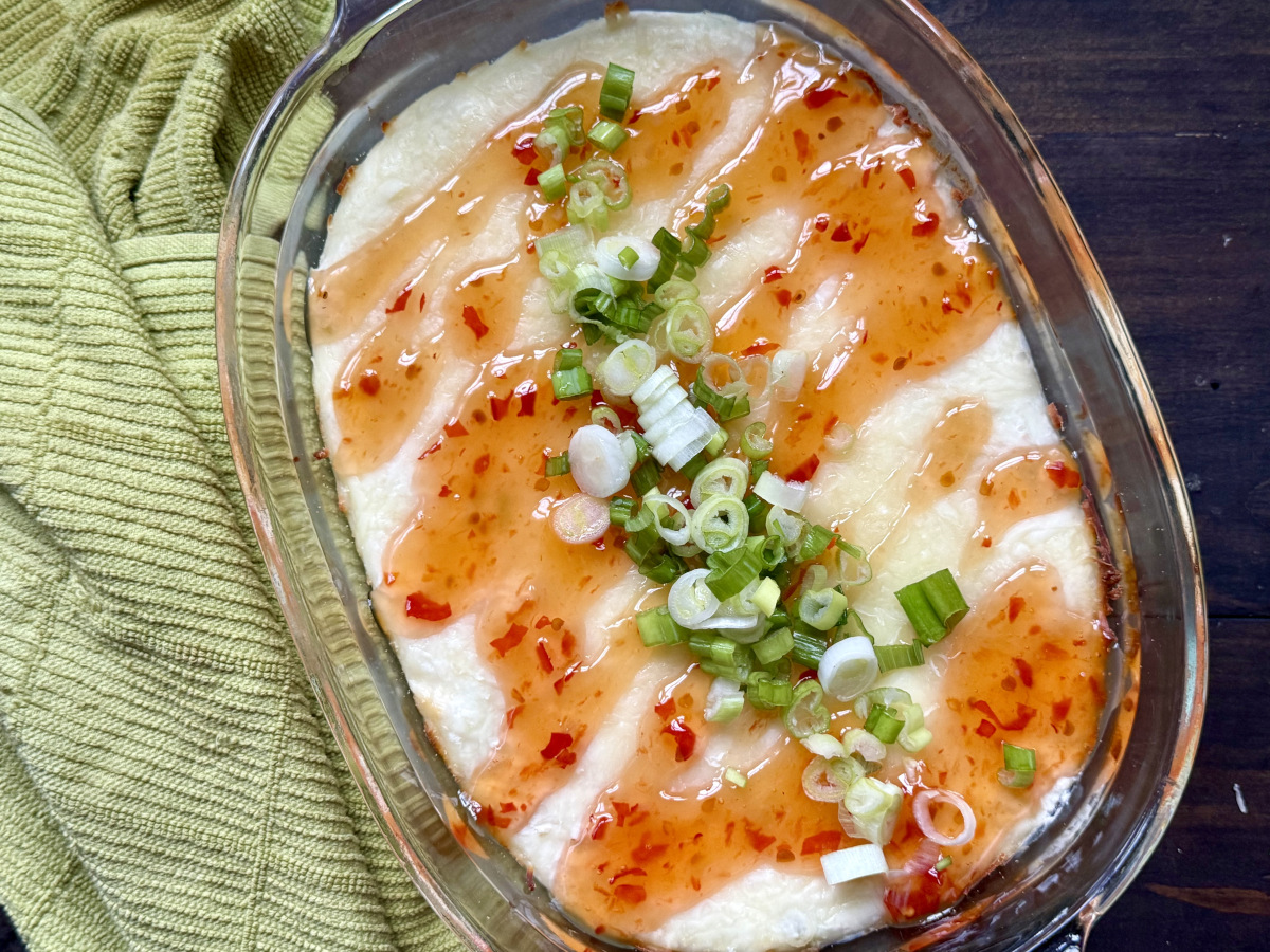 Healthy crab rangoon dip with chili sauce drizzled on top and garnished with green onions.