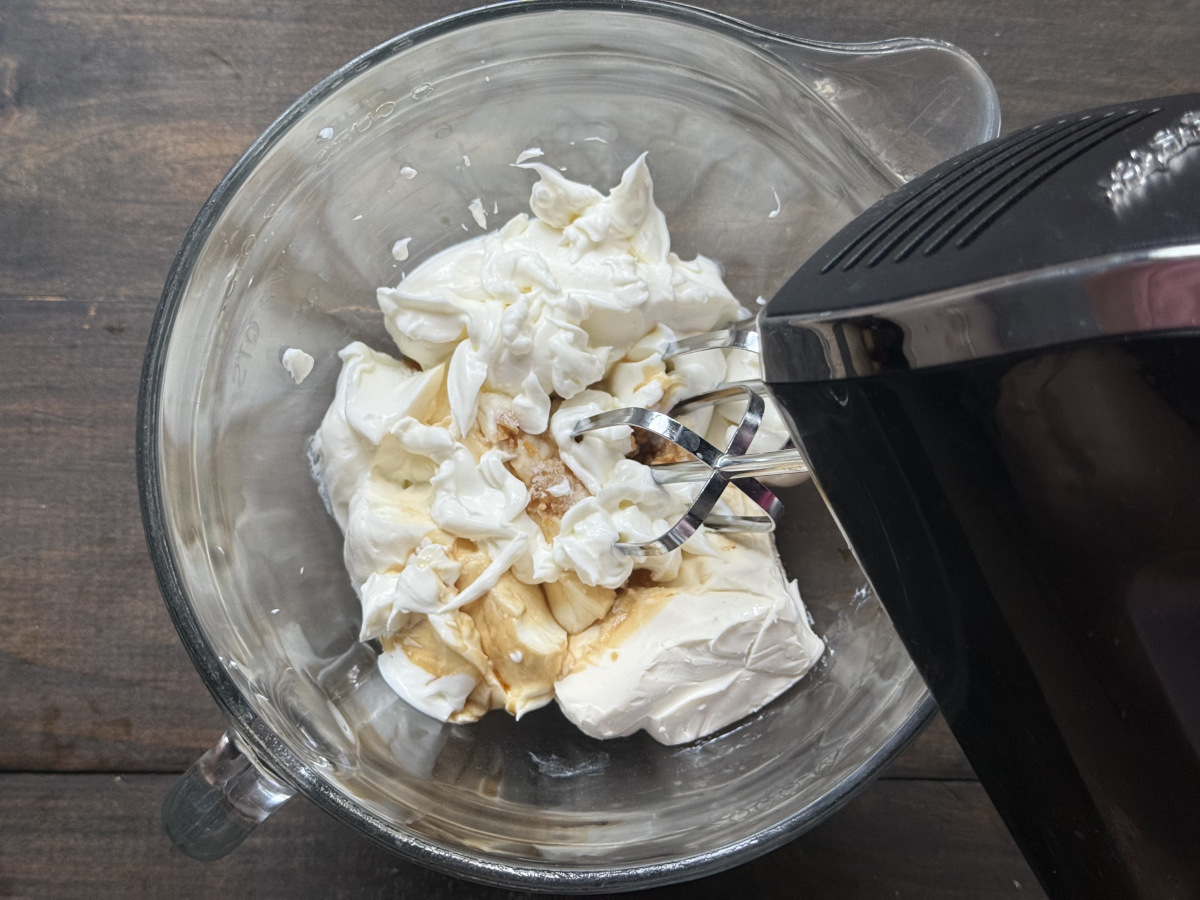 The ingredients in a bowl with a hand mixer to blend them.