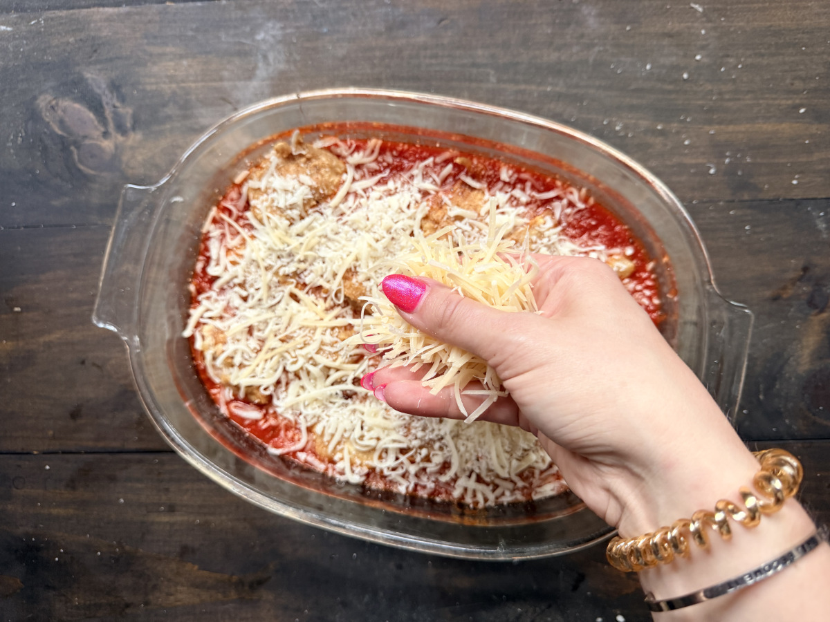 Cheese being added to the meatballs in the tray of sauce.