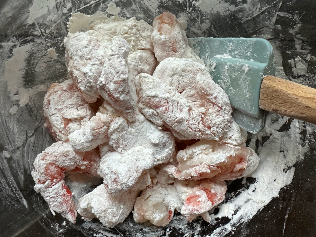 The shrimp and the flour being mixed with a rubber spatula.