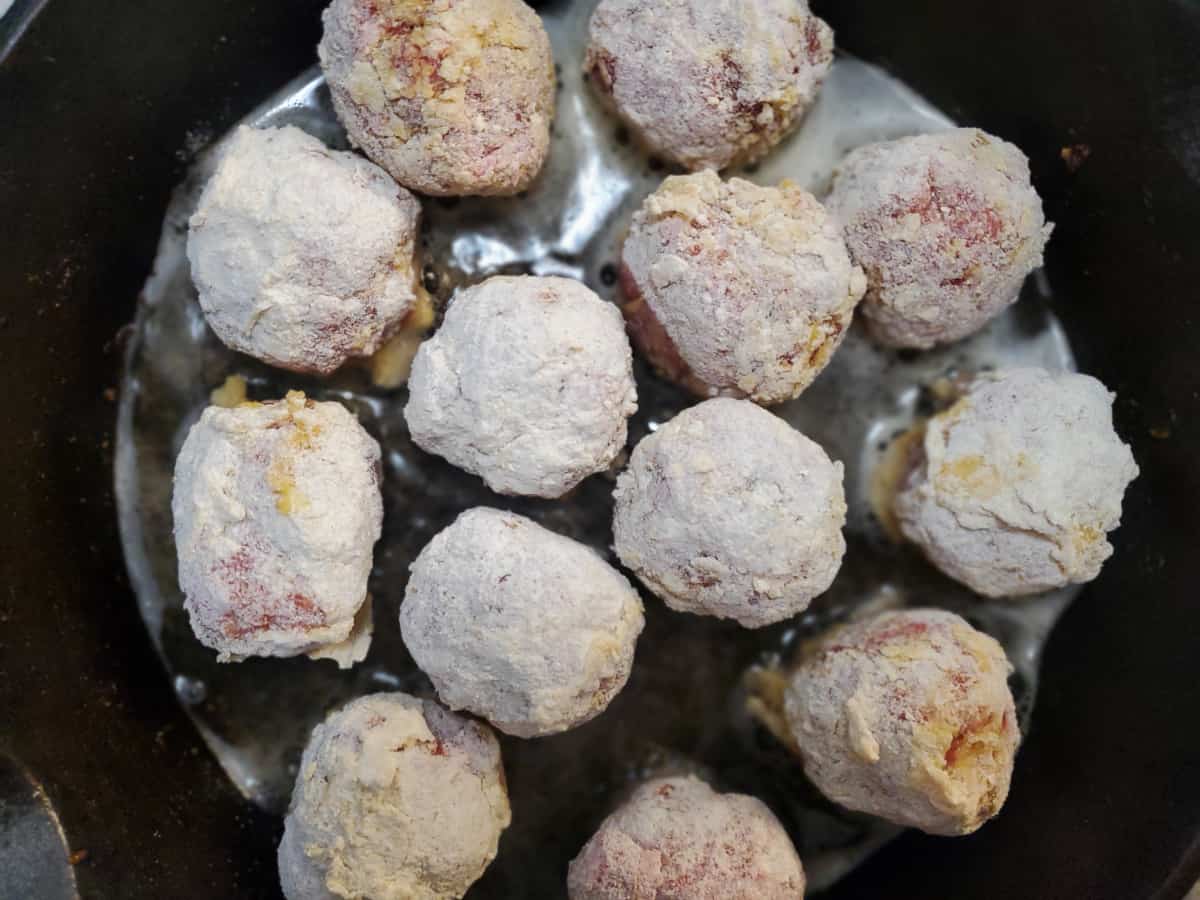 A batch of dredged meatballs frying in a pan.