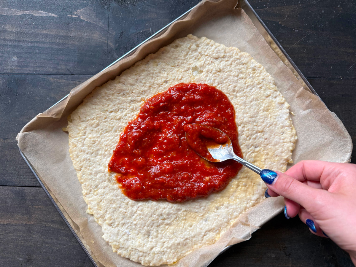 The sauce being spread over the baked crust.