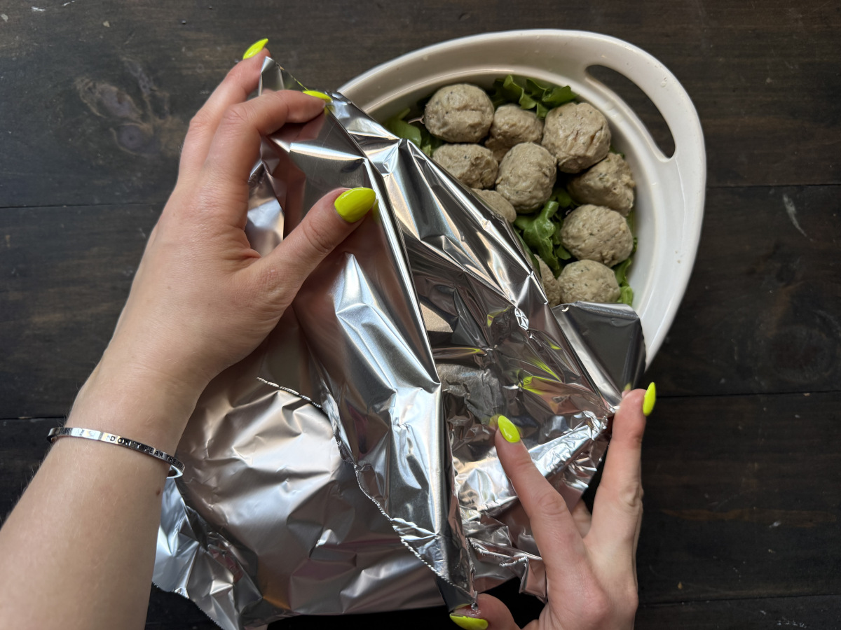 Hands covering the casserole dish with foil.