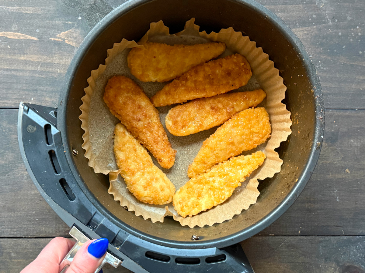 The chicken tenders prepared to cook inside an air fryer basket.
