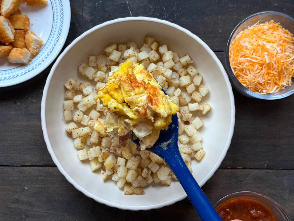 The ingredients laid out to the sides and the eggs being spooned onto the hash browns.