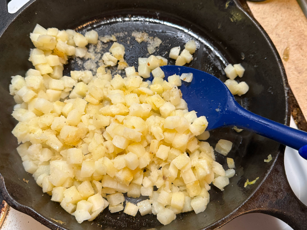 The hash browns cooking in a skillet with a blue spatula.