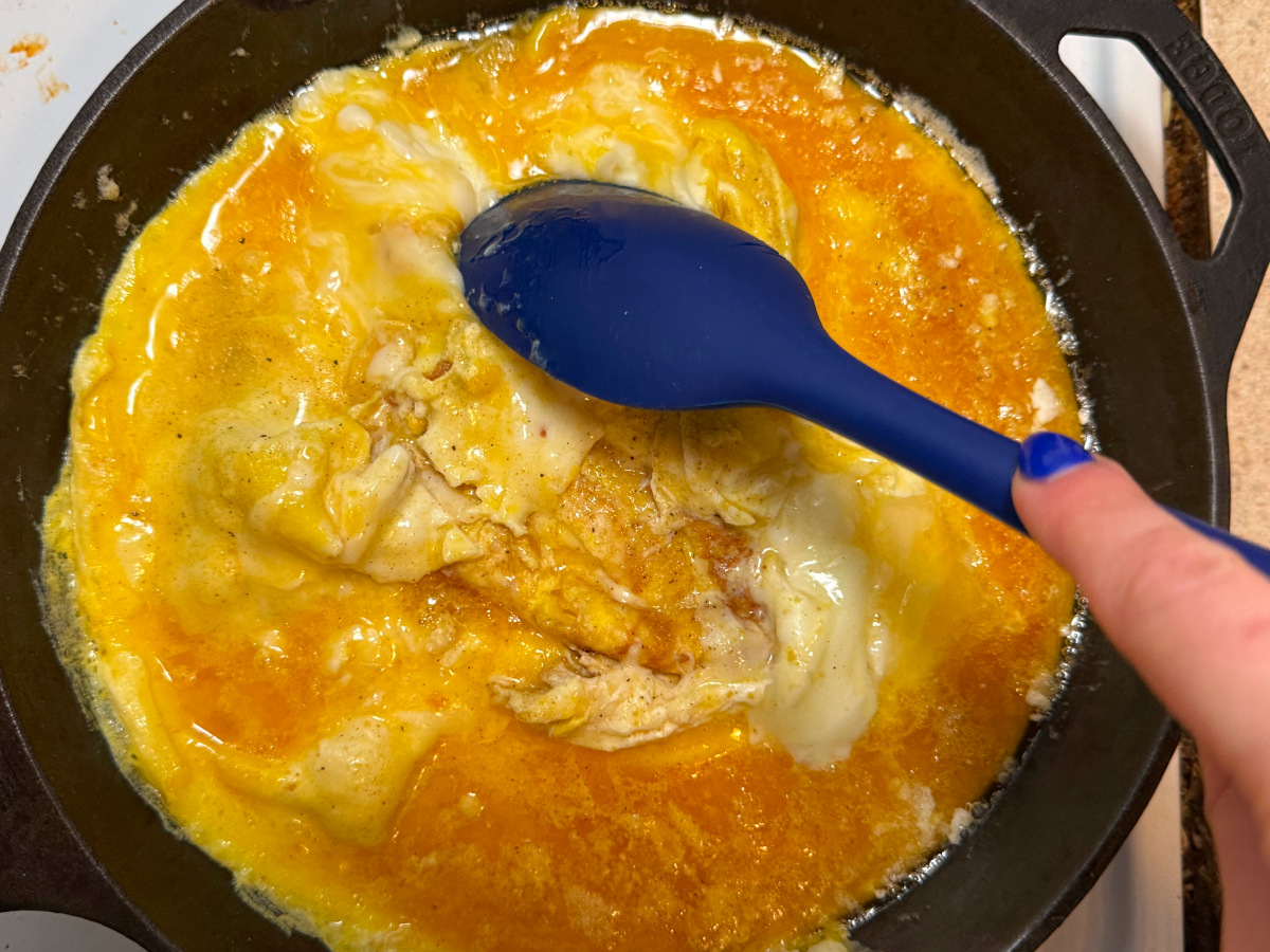 Scrambling the eggs in a skillet with a blue spatula.