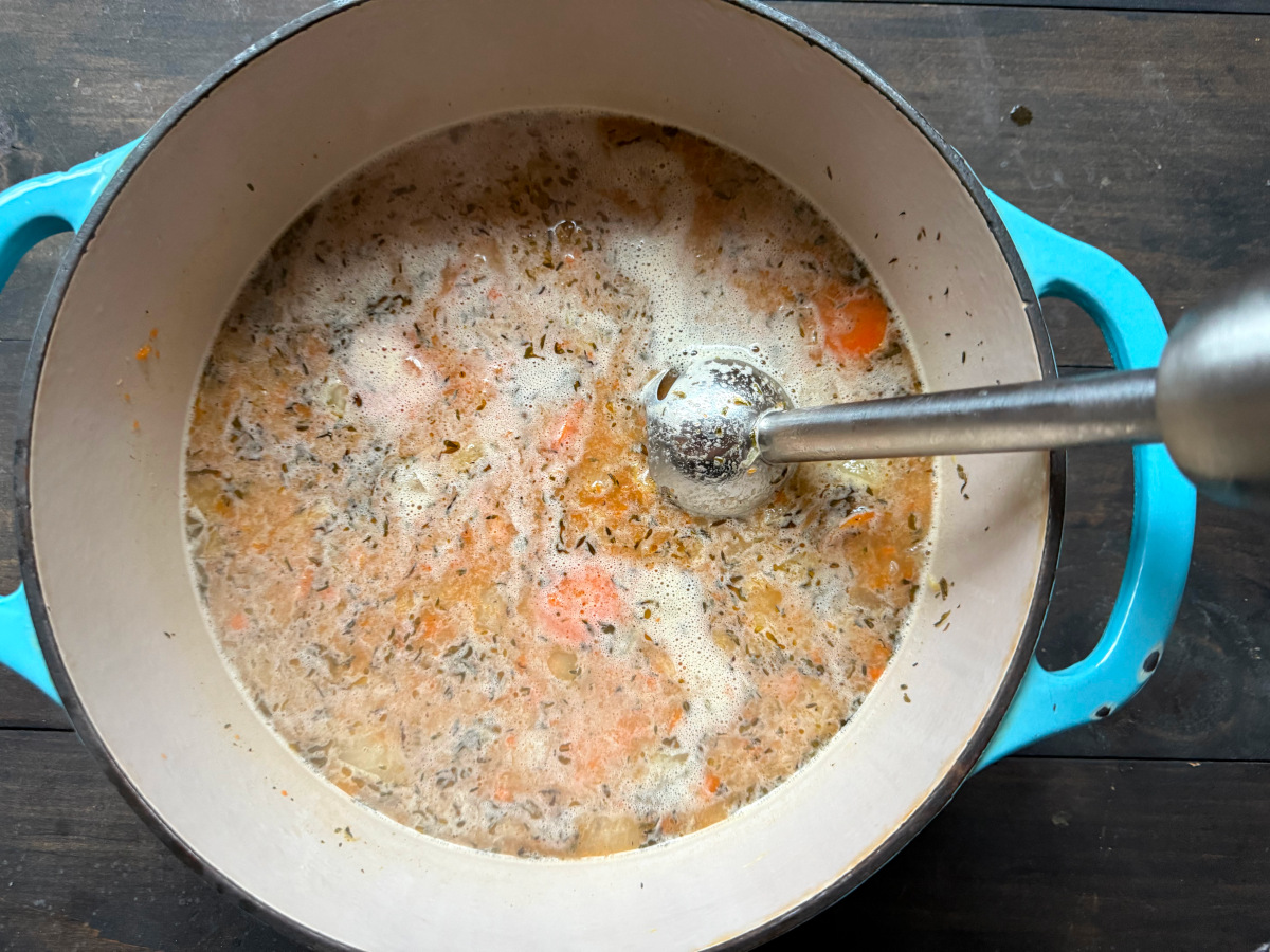 Soup in a dish being blended with an immersion blender.