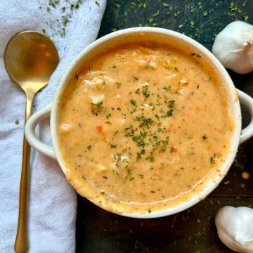 A bowl of roasted garlic soup with a spoon and veggies on the side.